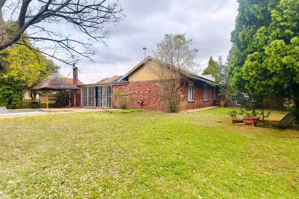 Rear view of the property featuring a brick facade, a swimming pool, and a thatched lapa set within a spacious garden area.