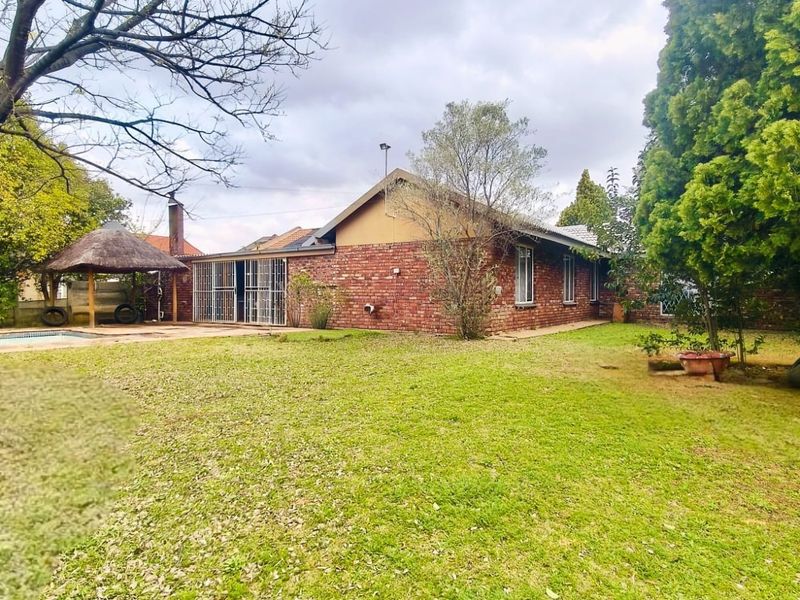 Rear view of the property featuring a brick facade, a swimming pool, and a thatched lapa set within a spacious garden area.