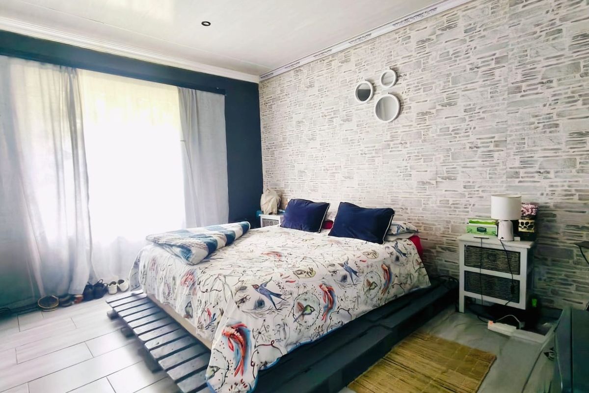 A bedroom featuring tiled flooring, recessed downlights, and a textured feature wall, providing a functional space with natural light.