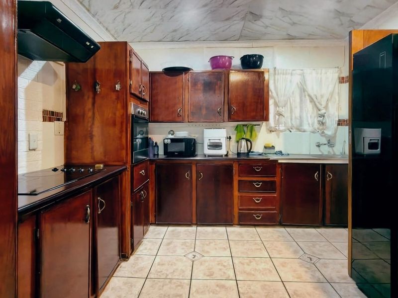 A functional kitchen featuring dark wood cabinetry, built-in oven, extractor fan, and tiled flooring, offering a traditional layout with potential for modern updates.