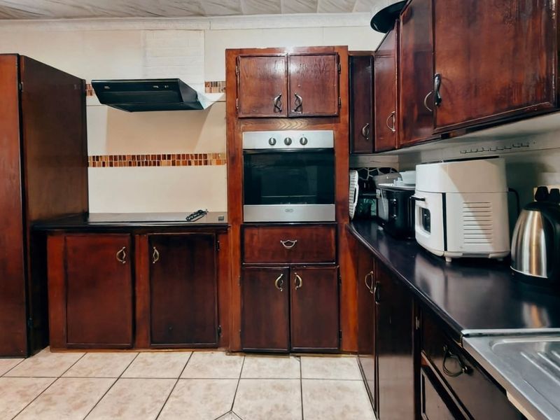 A functional kitchen featuring dark wood cabinetry, built-in oven, extractor fan, and tiled flooring, offering potential for a modern cosmetic update.