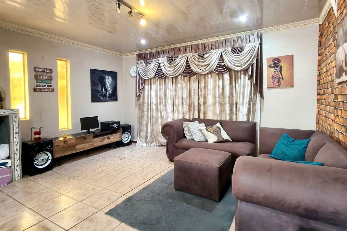 A living room featuring tiled flooring, an exposed brick accent wall, recessed wall niches, and coved ceiling details with track lighting.