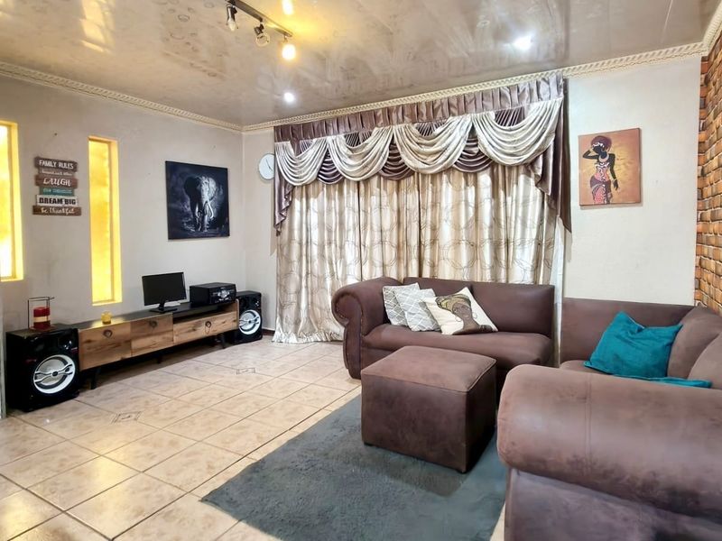 A living room featuring tiled flooring, an exposed brick accent wall, recessed wall niches, and coved ceiling details with track lighting.