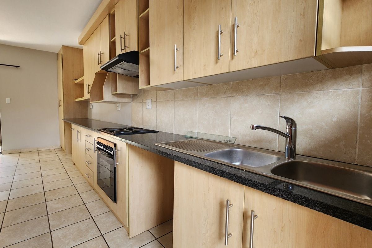A clean, functional kitchen featuring light wood cabinetry, granite countertops, a built-in oven, and a stainless steel double sink with tiled backsplash.