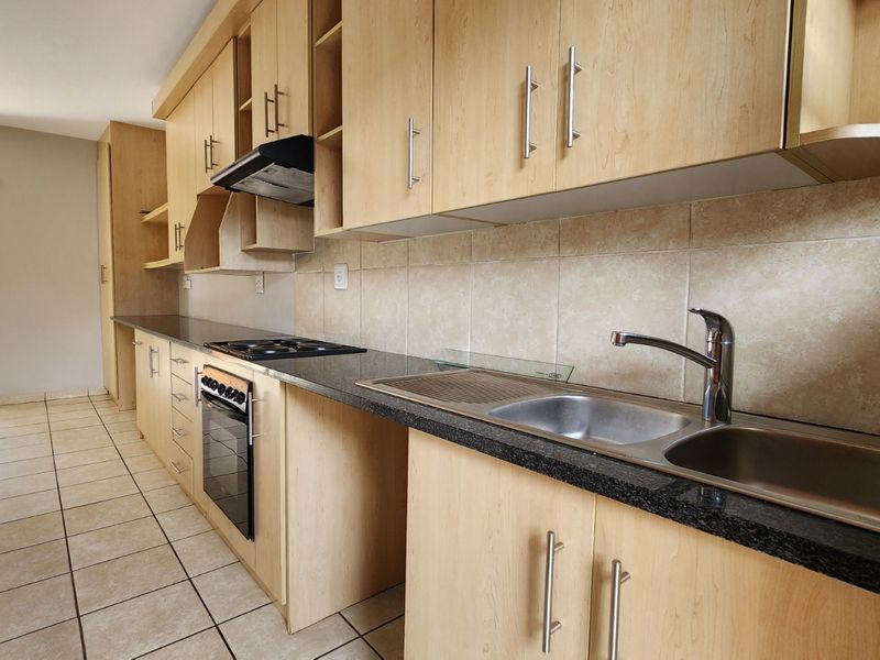 A clean, functional kitchen featuring light wood cabinetry, granite countertops, a built-in oven, and a stainless steel double sink with tiled backsplash.