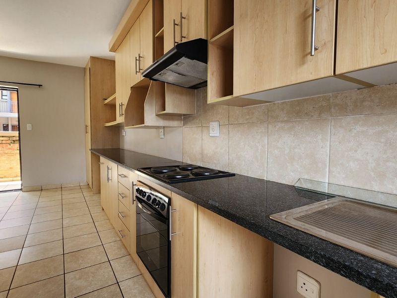A functional kitchen featuring light wood cabinetry, dark granite countertops, built-in oven and hob, and tiled flooring, with direct access to an outdoor balcony.