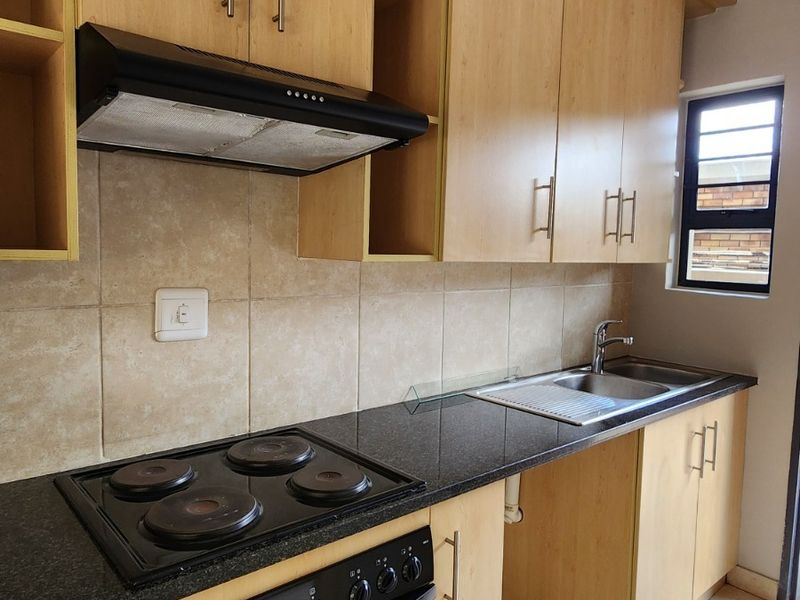 A functional kitchen featuring light wood cabinetry, granite countertops, a built-in oven with hob, extractor fan, and tiled finishes throughout.