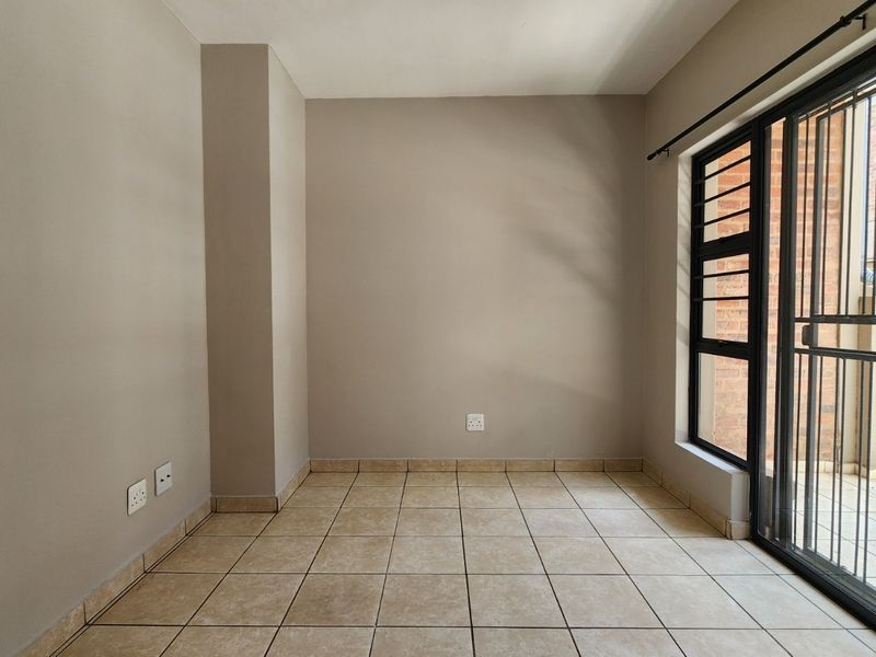 An empty, neutral-toned living area featuring tiled flooring and a sliding door with an integrated security gate, providing access to the exterior.