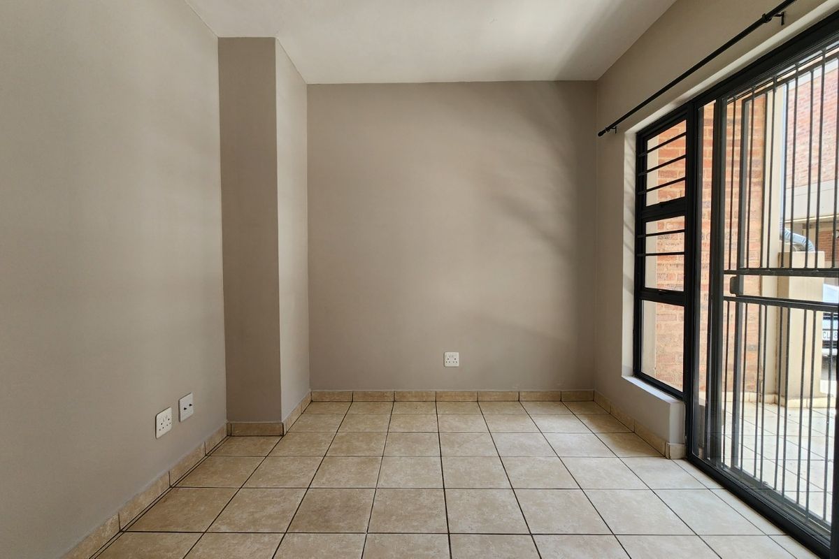 An empty, neutral-toned living area featuring tiled flooring and a sliding door with an integrated security gate, providing access to the exterior.
