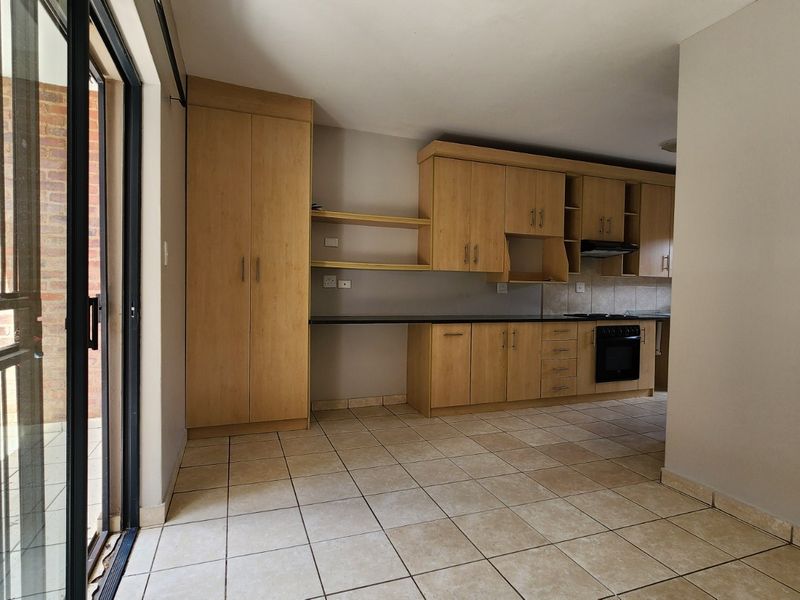 A functional kitchen featuring light wood cabinetry, built-in oven, extractor fan, and tiled flooring, with direct access to an outdoor patio area.