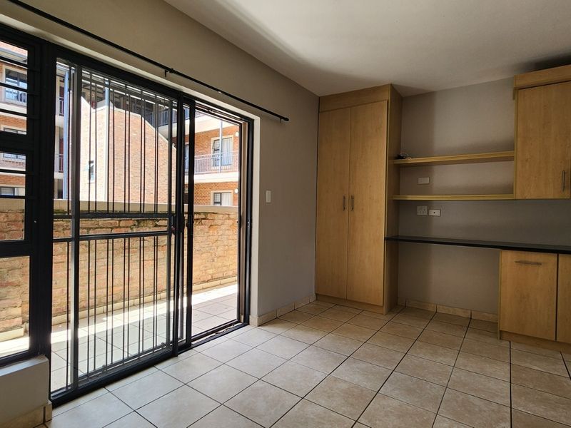 An open-plan living area featuring tiled flooring, built-in cabinetry with a workspace, and a sliding glass door leading to an outdoor patio.
