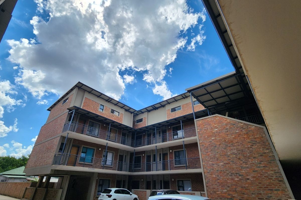 A multi-story apartment building featuring exposed brickwork, metal balcony railings, and covered exterior walkways under a clear blue sky.