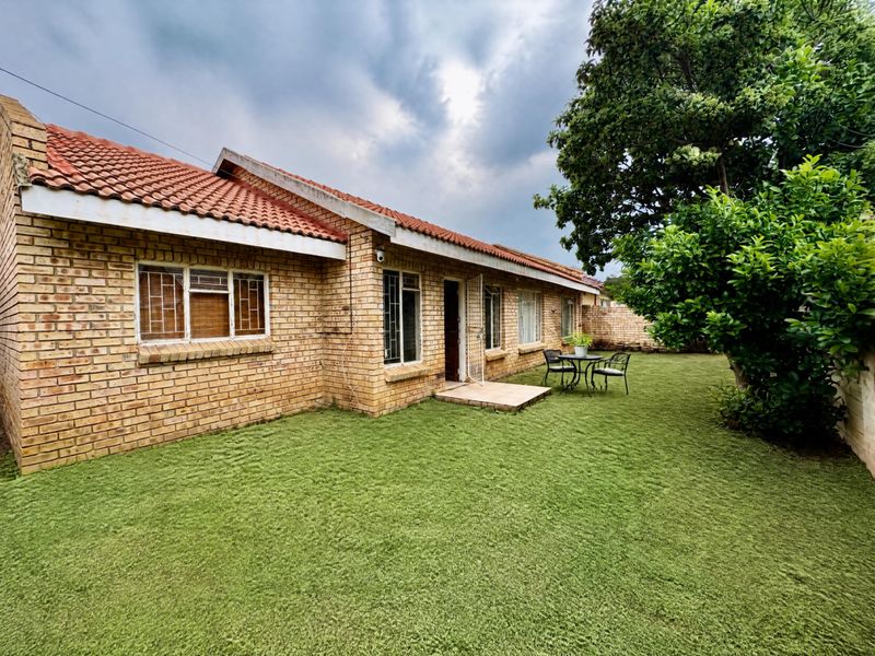 Rear view of the property featuring a face brick facade, terracotta roof tiles, and a well-maintained lawn with a small patio area.