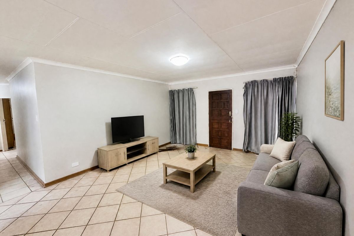 A spacious living room featuring neutral tiled flooring, a timber entrance door, and simple ceiling finishes, offering a clean and functional living space.