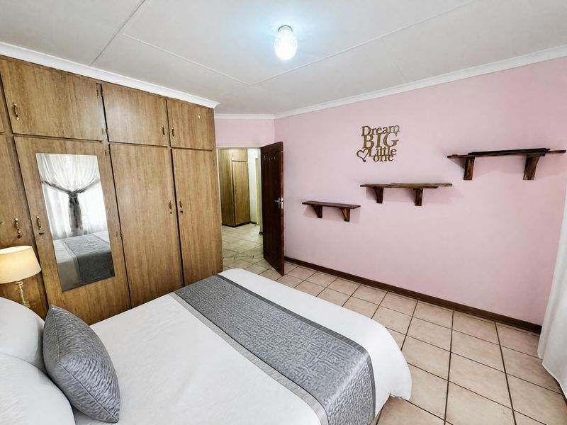 A bedroom featuring built-in wooden cupboards, tiled flooring, and pink painted walls, offering a functional space with ample storage.