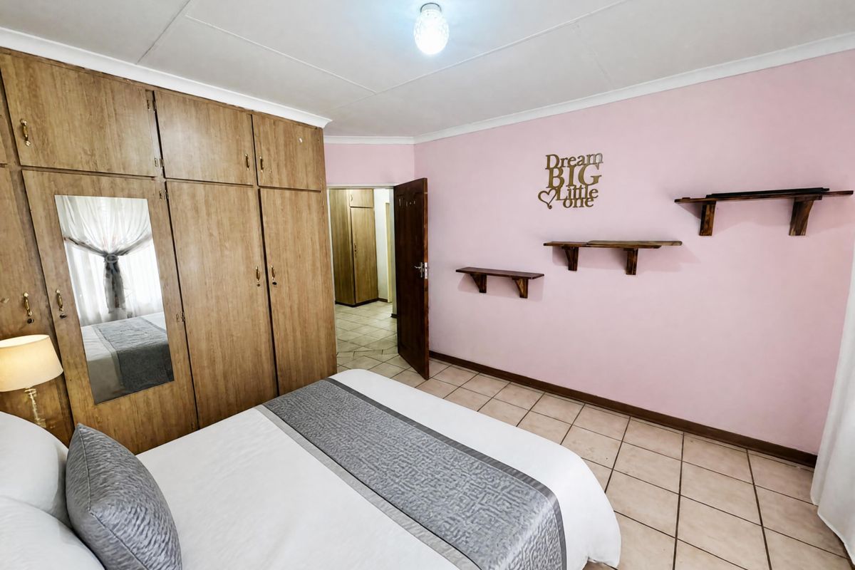 A bedroom featuring built-in wooden cupboards, tiled flooring, and pink painted walls, offering a functional space with ample storage.