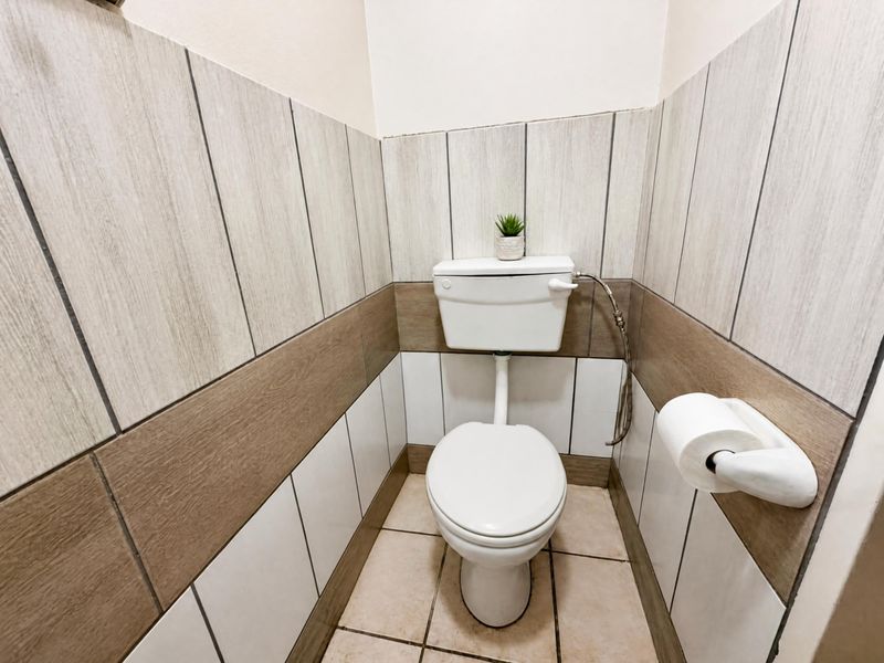 A compact guest bathroom featuring neutral-toned ceramic wall and floor tiles with a standard white toilet suite.
