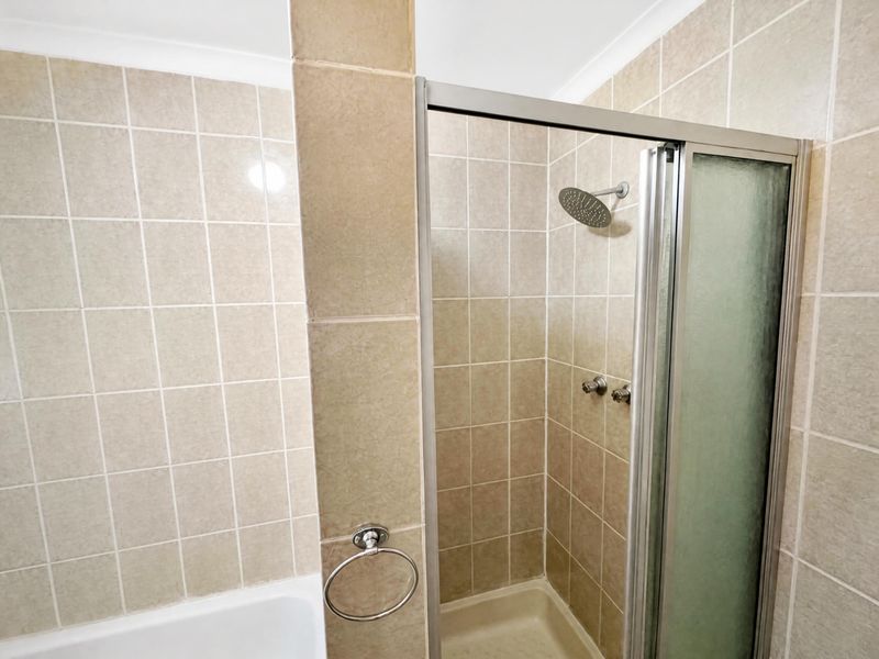 A functional bathroom featuring a tiled shower enclosure with a glass door, a bathtub, and a wall-mounted towel ring.