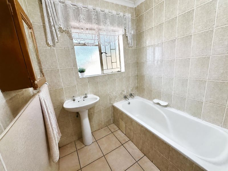 A functional bathroom featuring a pedestal basin, a built-in bathtub, and full-height ceramic wall tiling.