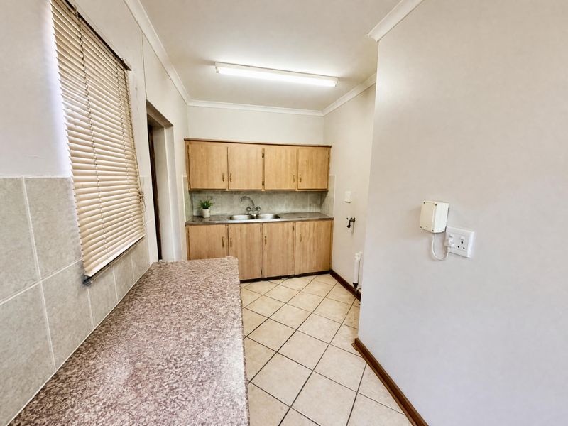 A functional laundry room featuring laminate cabinetry, a stainless steel sink, tiled splashback, and durable ceramic floor tiles.