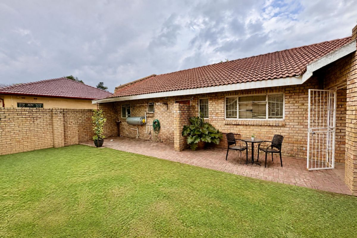 Rear view of the property featuring a brick facade, tiled roof, paved patio area, and a well-maintained lawn.