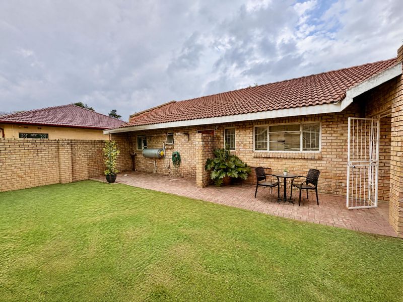 Rear view of the property featuring a brick facade, tiled roof, paved patio area, and a well-maintained lawn.