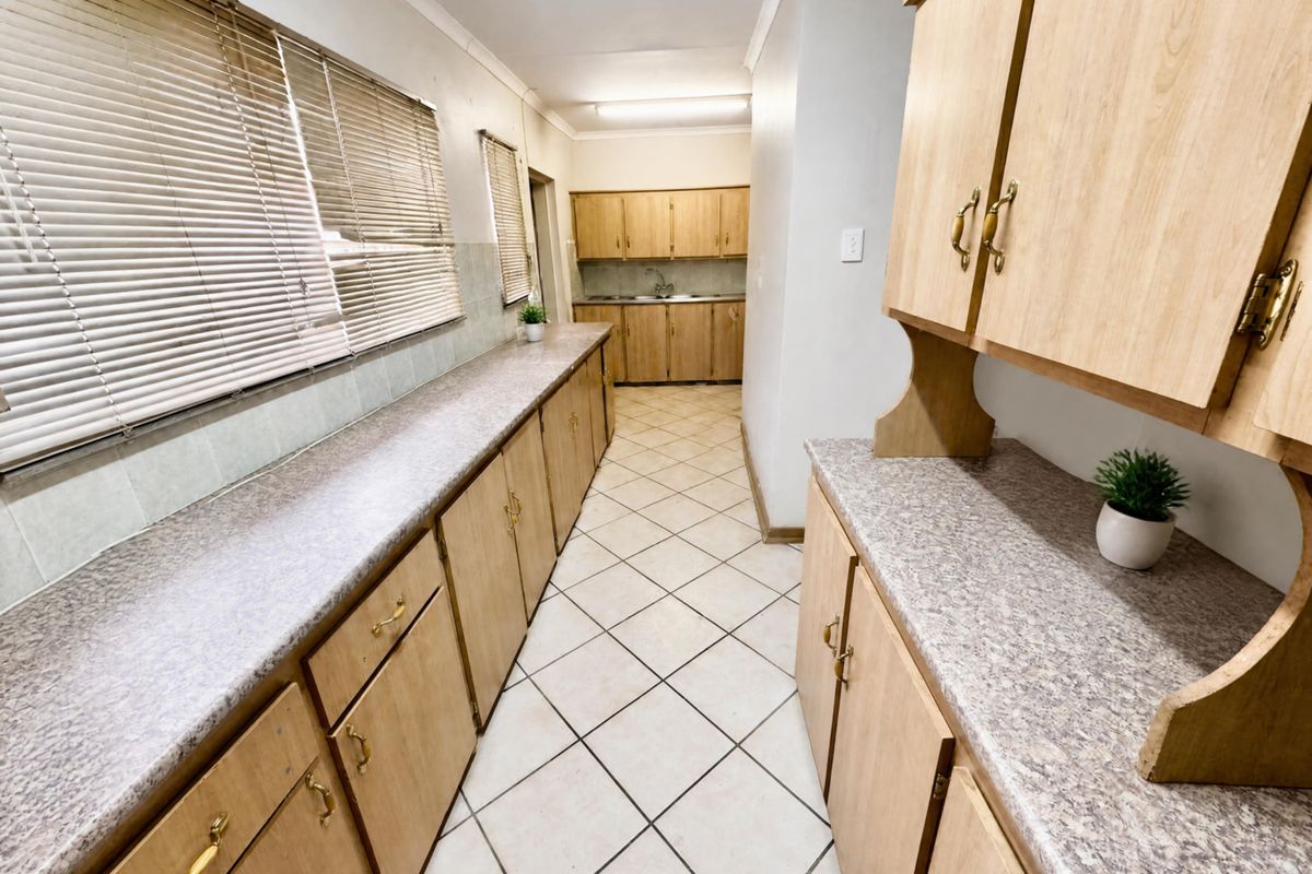 A functional kitchen featuring extensive laminate cabinetry, ample countertop workspace, tiled flooring, and a stainless steel sink, offering a clean and practical layout.