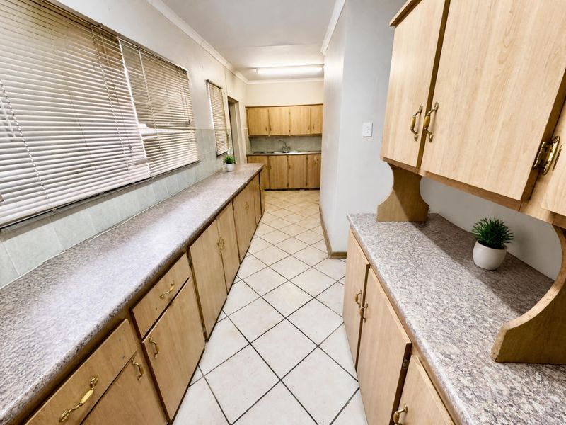 A functional kitchen featuring extensive laminate cabinetry, ample countertop workspace, tiled flooring, and a stainless steel sink, offering a clean and practical layout.