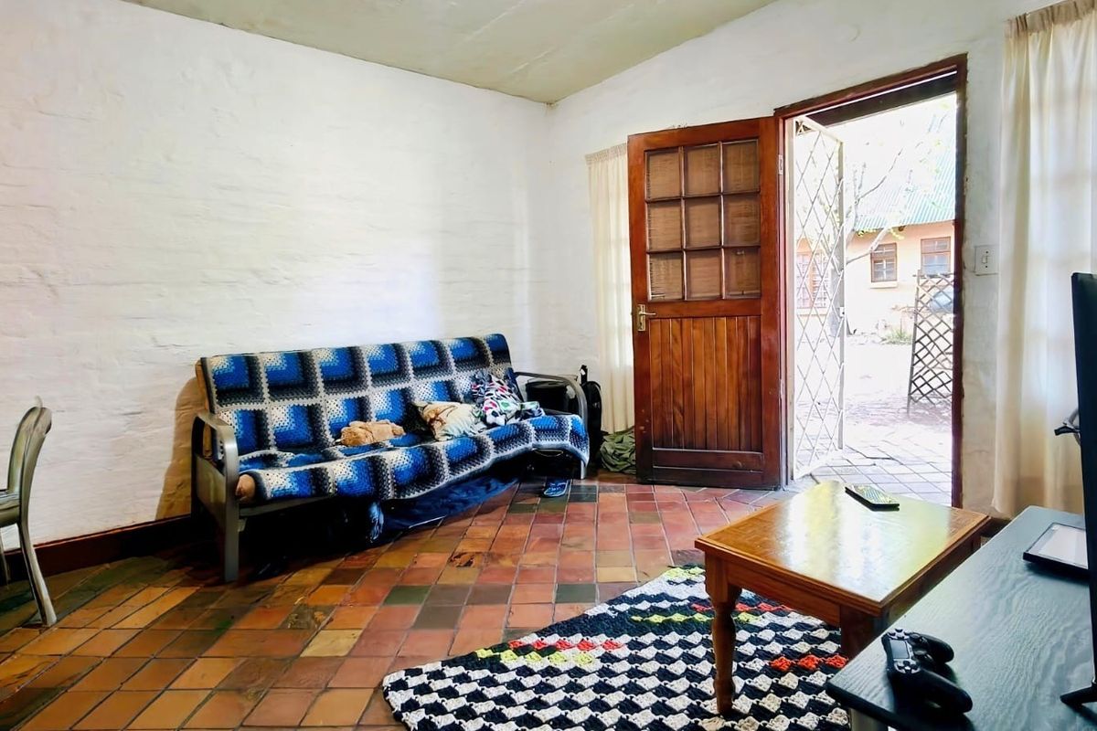 A living room featuring rustic terracotta tile flooring, textured white walls, and a timber door providing direct access to the exterior.
