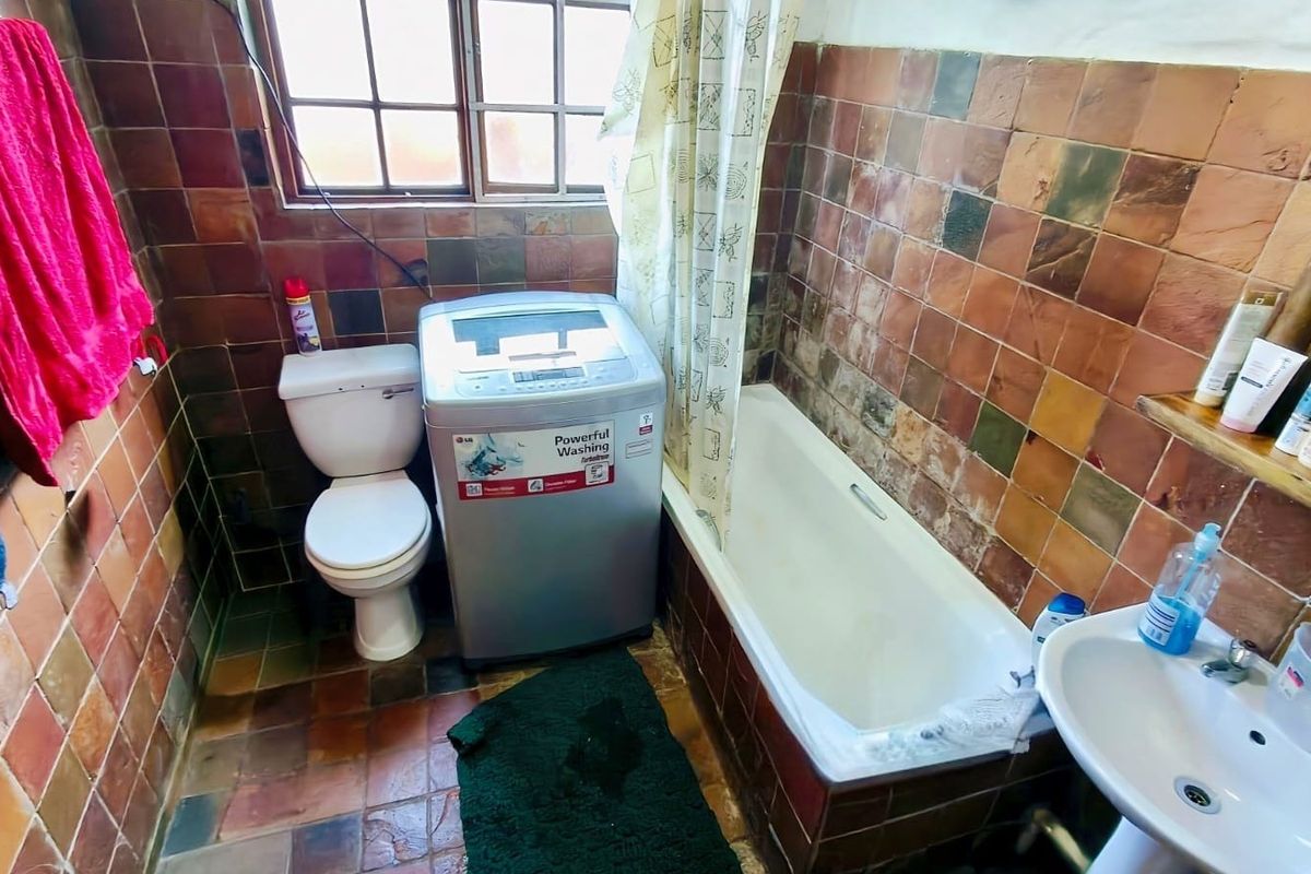 A compact bathroom featuring a bathtub, pedestal basin, and toilet with dated tiled finishes throughout.