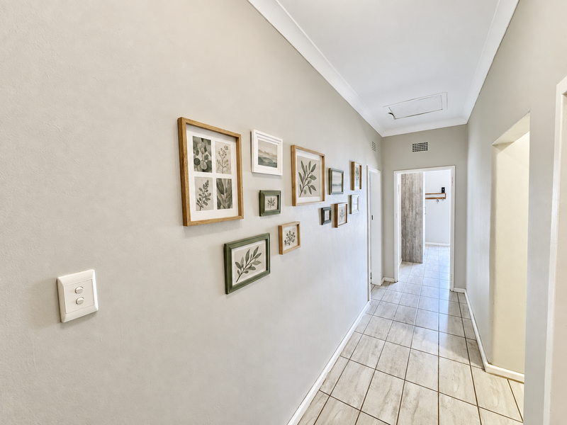 A bright and well-maintained hallway featuring neutral walls, tiled flooring, and a ceiling access hatch.