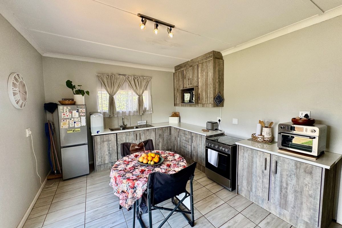 A functional kitchen featuring wood-look laminate cabinetry, tiled flooring, built-in oven and hob, and a stainless steel sink with a window view.