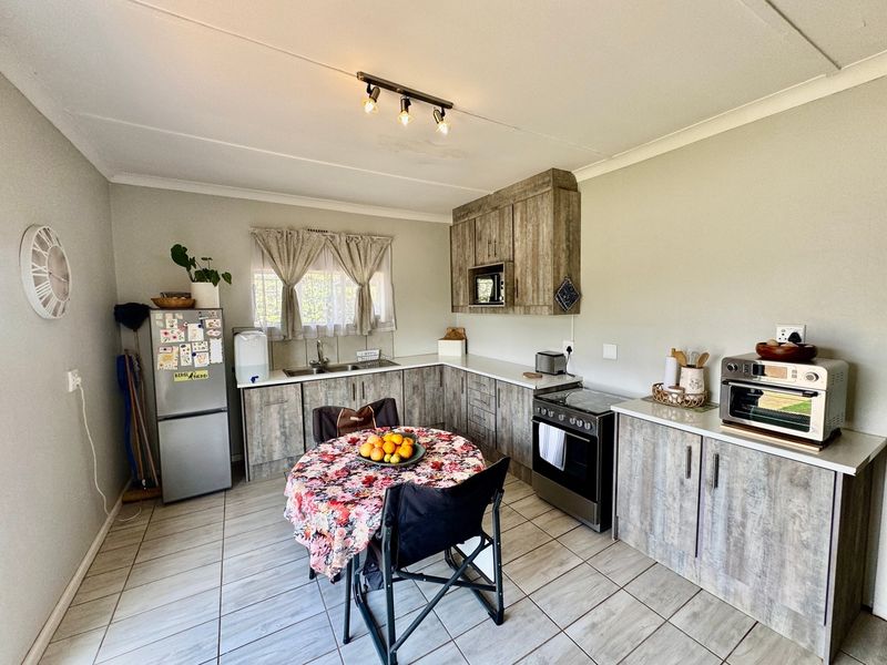 A functional kitchen featuring wood-look laminate cabinetry, tiled flooring, built-in oven and hob, and a stainless steel sink with a window view.