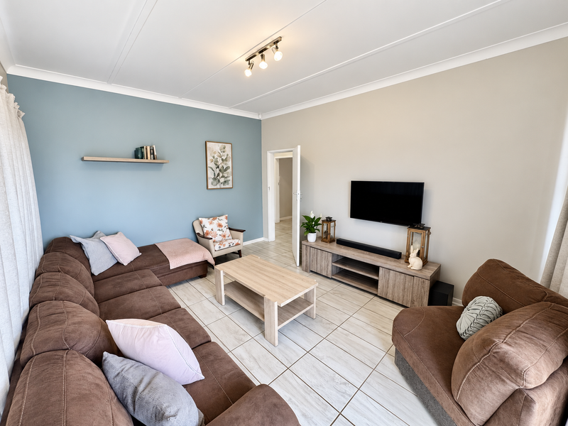A well-maintained living room featuring neutral tiled flooring, a feature wall with a floating shelf, and modern ceiling track lighting.