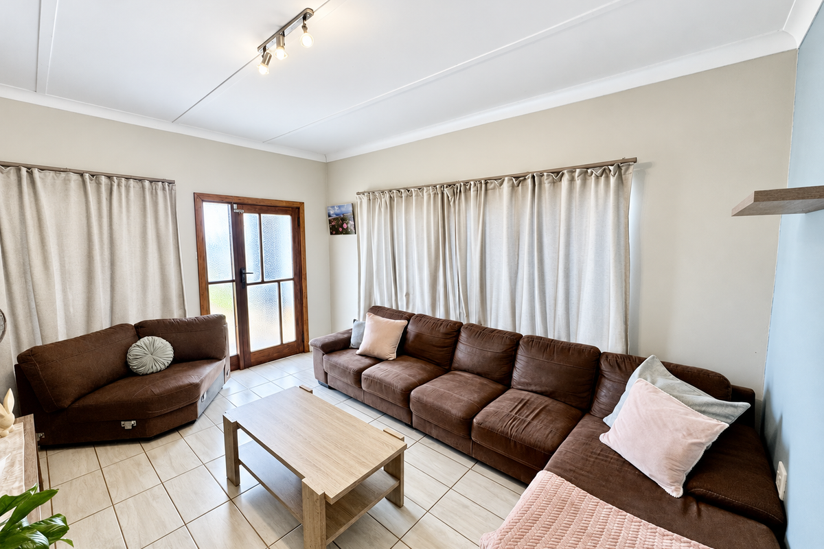 A bright living room featuring neutral walls, tiled flooring, and a timber-framed glass door providing access to the exterior.