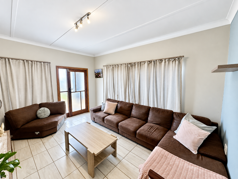 A bright living room featuring neutral walls, tiled flooring, and a timber-framed glass door providing access to the exterior.