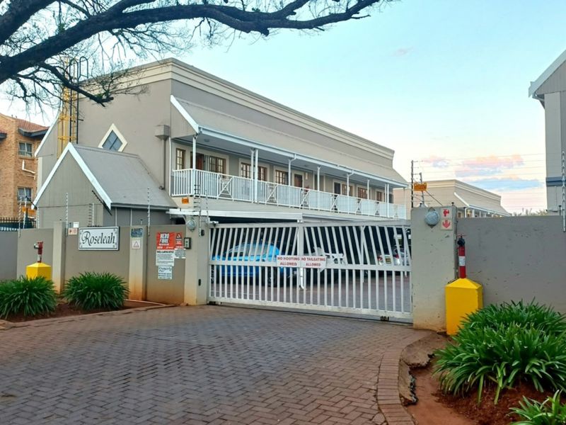 Front exterior view of the Roseleah apartment complex, featuring a secure gated entrance, paved driveway, and upper-level balcony access.