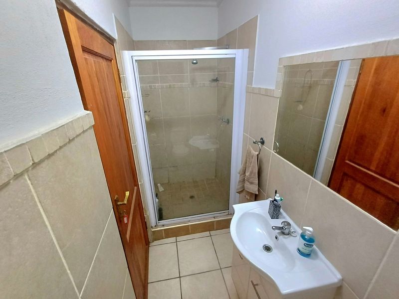 A functional bathroom featuring a shower enclosure, vanity basin, and neutral wall tiling with timber door access.
