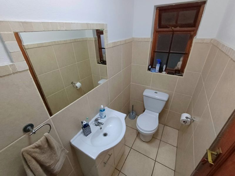 A compact bathroom featuring tiled walls and flooring, a pedestal vanity with a basin, and a timber-framed window.