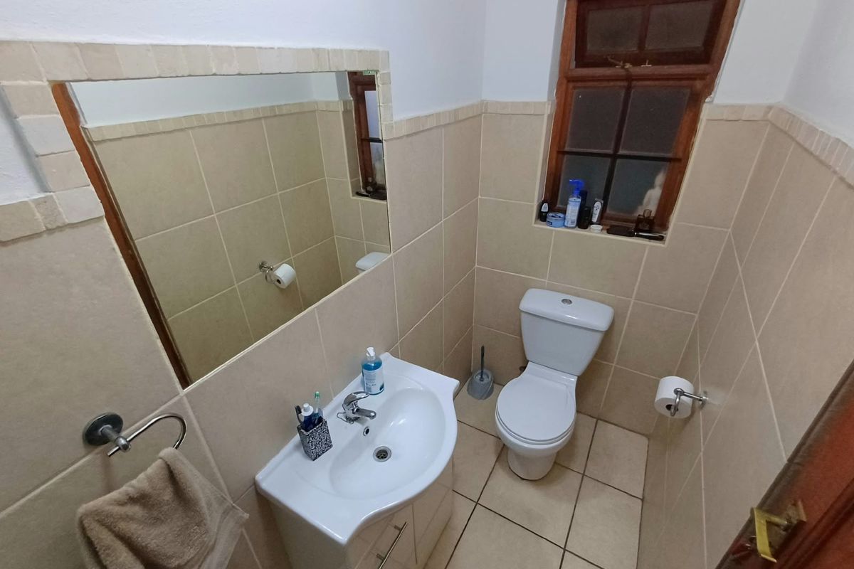 A compact bathroom featuring tiled walls and flooring, a pedestal vanity with a basin, and a timber-framed window.