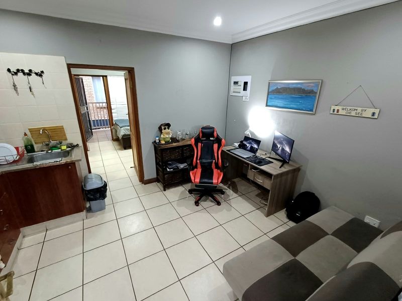 Open-plan living area featuring tiled flooring, a compact kitchen kitchenette, and direct access to an adjacent bedroom.