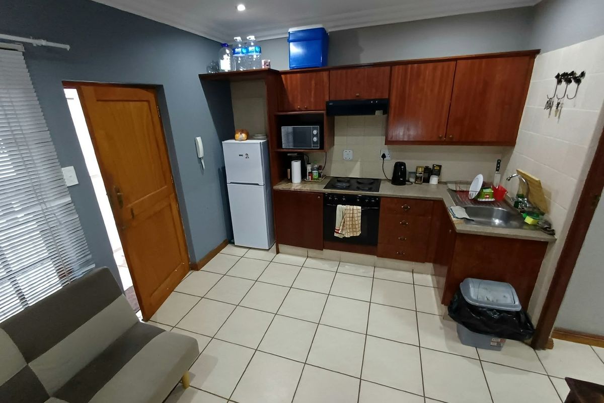 Compact kitchen featuring wooden cabinetry, built-in oven and hob, stainless steel sink, and tiled flooring in an open-plan layout.