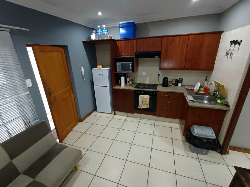 Compact kitchen featuring wooden cabinetry, built-in oven and hob, stainless steel sink, and tiled flooring in an open-plan layout.