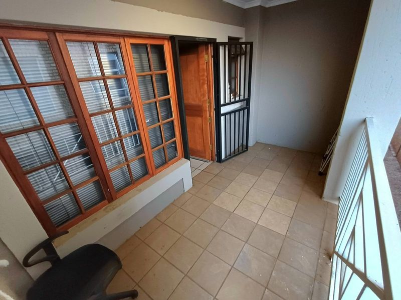 A covered balcony area featuring tiled flooring, timber-framed windows, and a security gate, providing a functional outdoor space for the apartment.