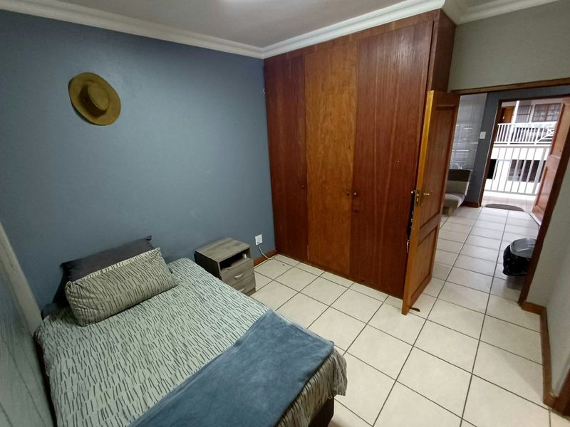 A bedroom featuring tiled flooring, a built-in wooden wardrobe, and coved ceiling cornices, with direct access to an adjacent hallway.