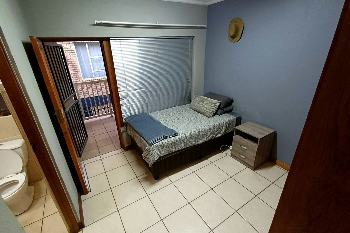 A compact bedroom featuring tiled flooring, venetian blinds, and direct access to an adjoining balcony and bathroom.
