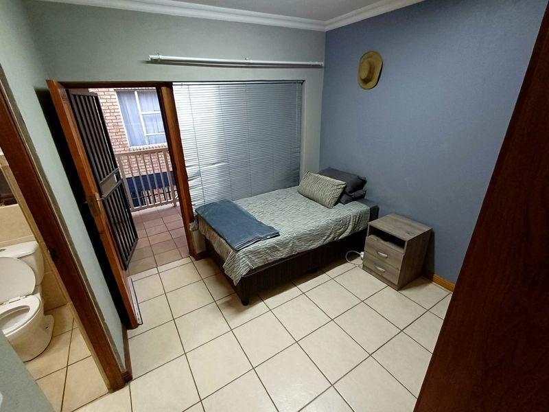 A compact bedroom featuring tiled flooring, venetian blinds, and direct access to an adjoining balcony and bathroom.