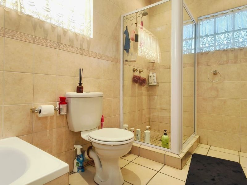 A functional bathroom featuring a tiled shower enclosure, toilet, and neutral wall tiling throughout.