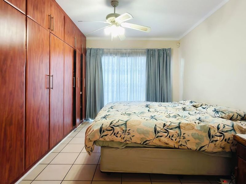 A bedroom featuring extensive floor-to-ceiling built-in wooden cupboards, tiled flooring, and a central ceiling fan with light fixture.