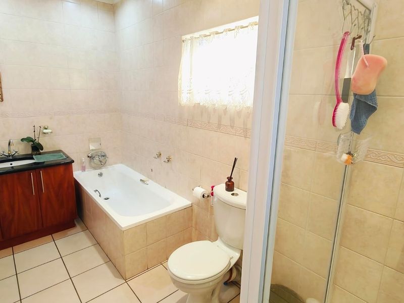 A functional bathroom featuring a vanity with integrated basin, a built-in bathtub, a toilet, and a separate shower enclosure with neutral wall and floor tiling.